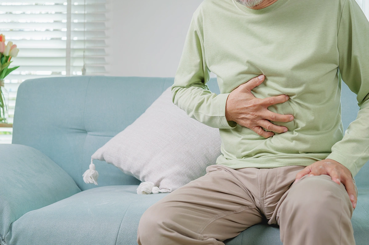 Older man clutching his abdomen with a pained expression, indicating stomach discomfort.